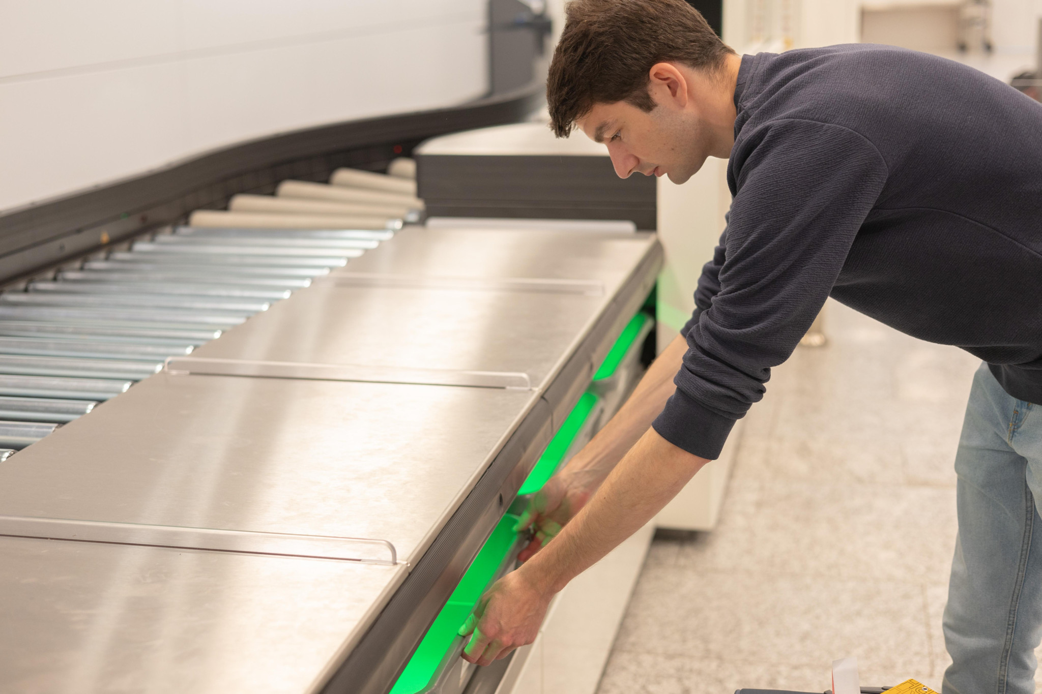 Mann beugt sich über eine moderne Maschine in einem industriellen Umfeld.